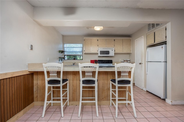 kitchen featuring cream cabinetry, a kitchen breakfast bar, light tile patterned flooring, and white appliances