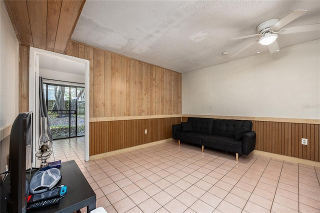 living area with a textured ceiling, ceiling fan, wooden walls, and light tile patterned flooring