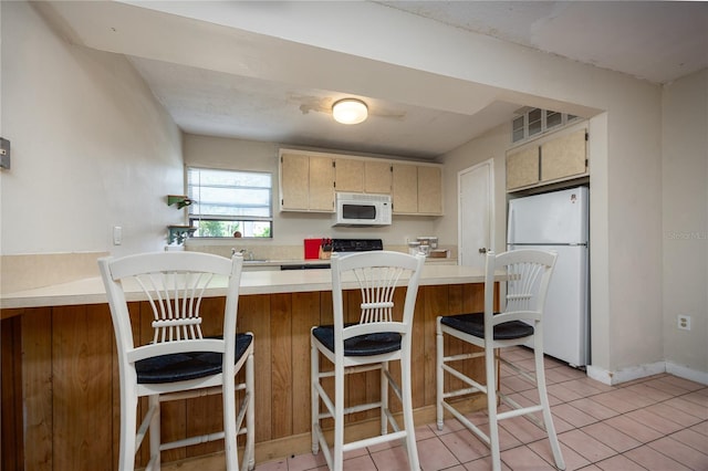 kitchen with white appliances, sink, cream cabinetry, light tile patterned flooring, and a kitchen bar