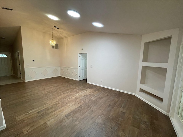 empty room featuring lofted ceiling, dark hardwood / wood-style flooring, and built in shelves