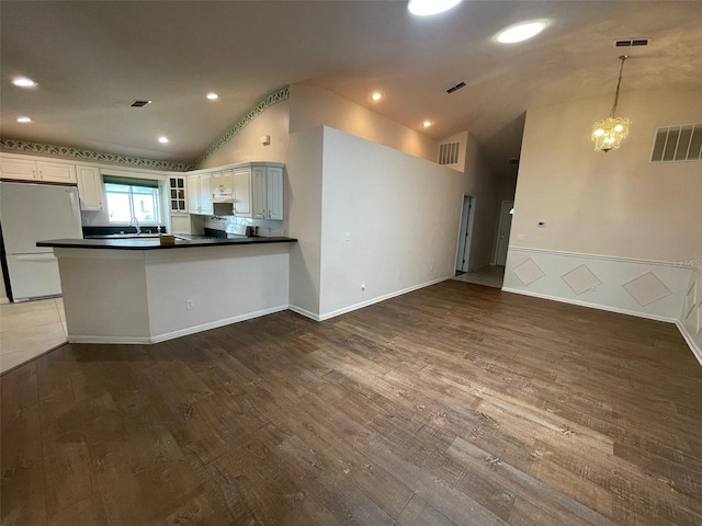 kitchen with vaulted ceiling, decorative light fixtures, white cabinets, white refrigerator, and kitchen peninsula