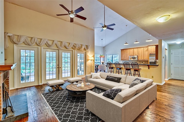 living room with light wood-type flooring, ceiling fan, a stone fireplace, french doors, and high vaulted ceiling