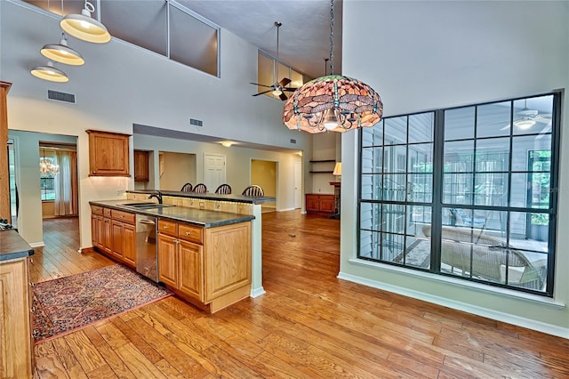 kitchen featuring light wood-type flooring, pendant lighting, a towering ceiling, kitchen peninsula, and stainless steel dishwasher