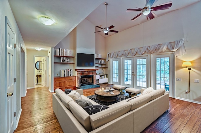 living room featuring a brick fireplace, french doors, hardwood / wood-style flooring, and ceiling fan