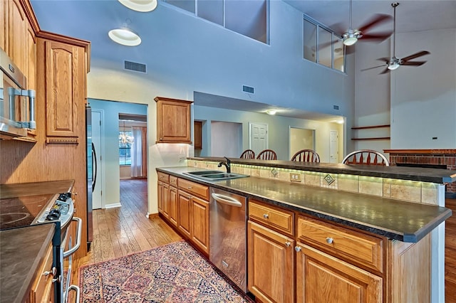 kitchen with sink, stainless steel appliances, a kitchen breakfast bar, a high ceiling, and light wood-type flooring