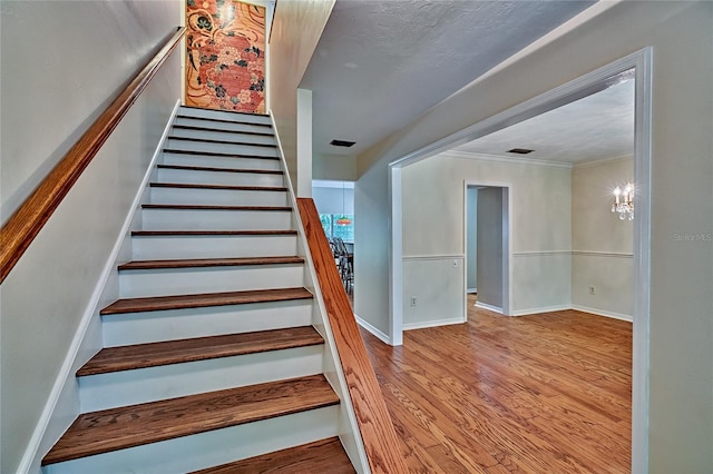 stairs with wood-type flooring, a chandelier, and ornamental molding