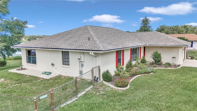 exterior space featuring a shingled roof, fence private yard, a lawn, and stucco siding