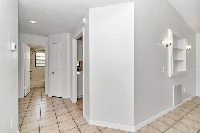 hallway featuring built in features, visible vents, baseboards, and light tile patterned flooring