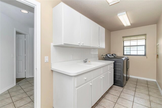 clothes washing area featuring light tile patterned floors, cabinet space, a sink, and washer and clothes dryer