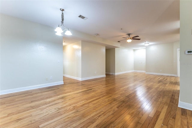 unfurnished room with ceiling fan with notable chandelier and light wood-type flooring