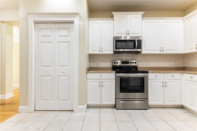 kitchen with appliances with stainless steel finishes, backsplash, white cabinetry, and light tile patterned flooring