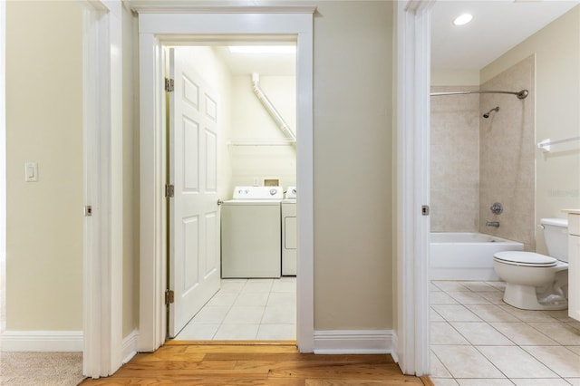 bathroom featuring washing machine and dryer, hardwood / wood-style floors, tiled shower / bath combo, and toilet