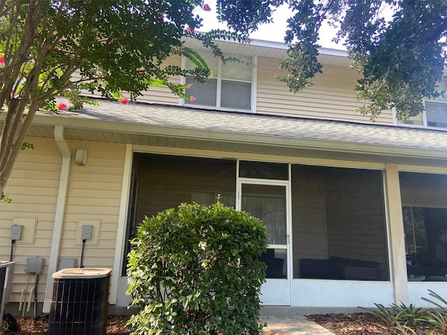 view of property exterior with central AC unit, a sunroom, and roof with shingles