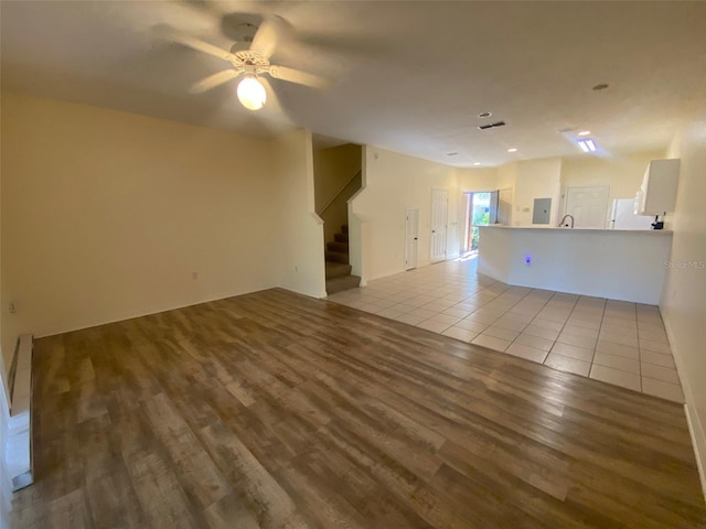 unfurnished living room with wood finished floors, ceiling fan, and stairway