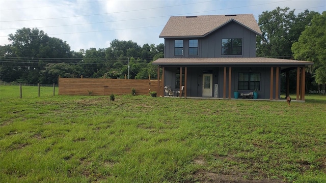 rear view of house featuring board and batten siding, fence, and a lawn