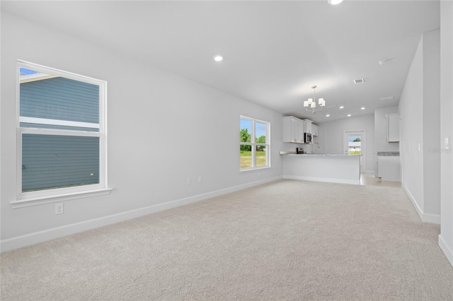 unfurnished living room featuring light colored carpet, sink, and a chandelier