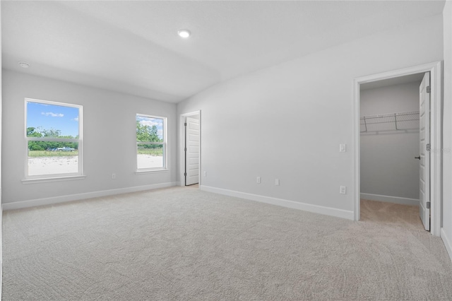 unfurnished bedroom with lofted ceiling, a spacious closet, light carpet, and a closet