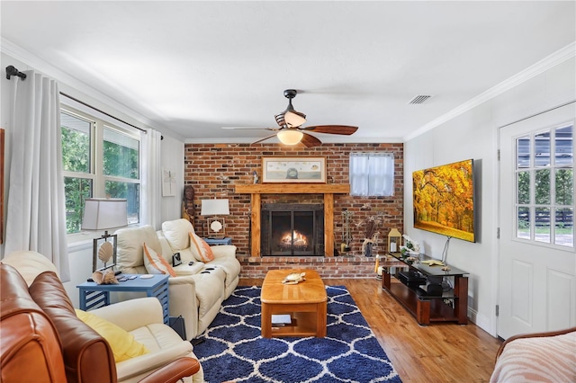 living room with crown molding, ceiling fan, a fireplace, light hardwood / wood-style floors, and brick wall