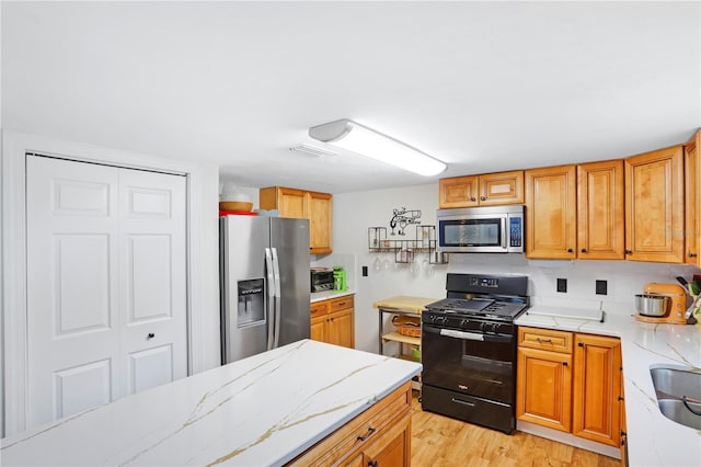 kitchen featuring light stone countertops, backsplash, sink, black appliances, and light hardwood / wood-style flooring