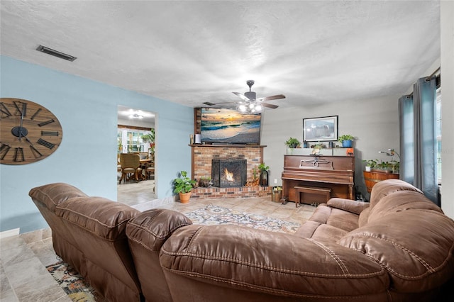 living room featuring ceiling fan, a brick fireplace, and a textured ceiling