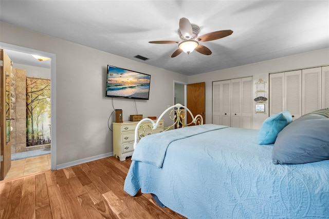 bedroom featuring multiple closets, ensuite bathroom, ceiling fan, and light wood-type flooring