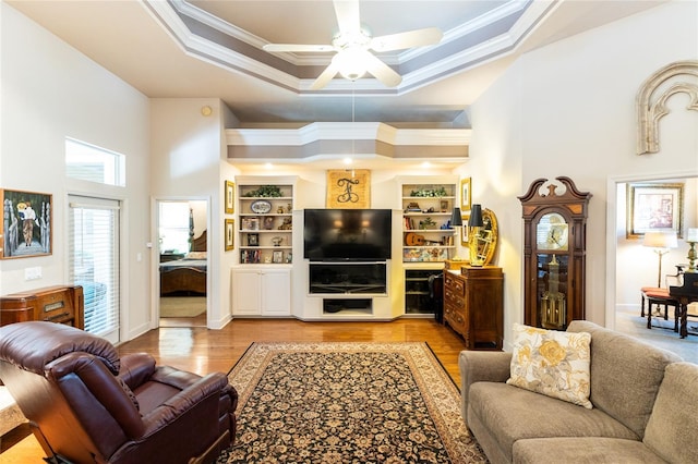 living room featuring a raised ceiling, crown molding, ceiling fan, and light wood-type flooring