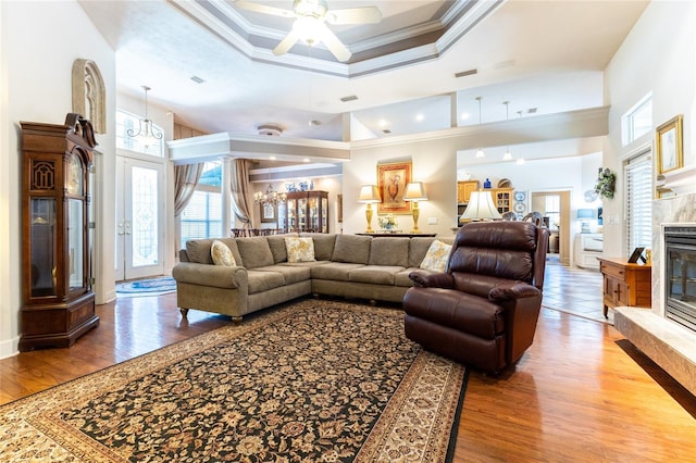 living room featuring crown molding, ceiling fan, a towering ceiling, a tray ceiling, and wood-type flooring