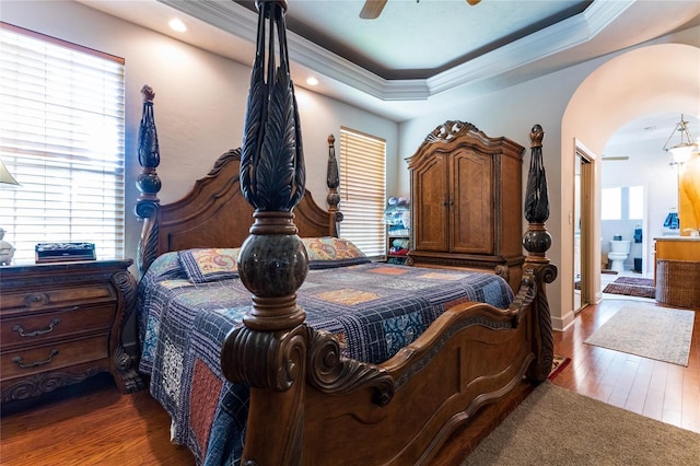 bedroom featuring a raised ceiling, crown molding, ceiling fan, connected bathroom, and dark hardwood / wood-style flooring