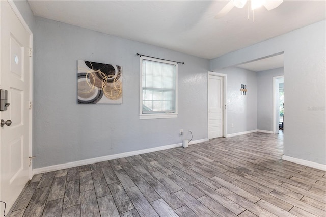 empty room featuring a healthy amount of sunlight, ceiling fan, baseboards, and wood finished floors