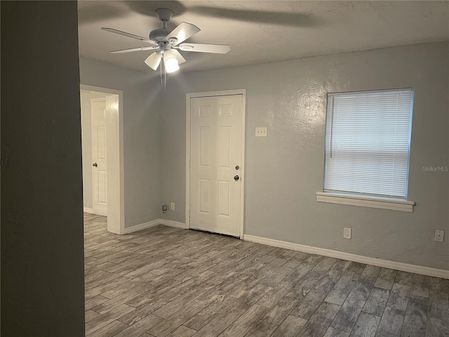 empty room with a textured wall, ceiling fan, baseboards, and wood finished floors