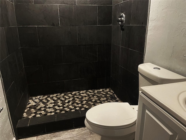 full bath featuring a tile shower, vanity, and toilet