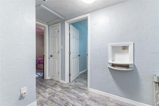 hallway featuring a textured wall, a textured ceiling, baseboards, and wood finished floors