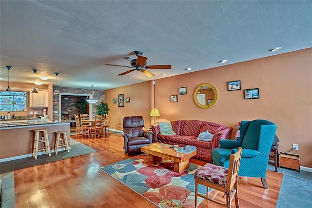 living room featuring ceiling fan, a textured ceiling, and light hardwood / wood-style flooring