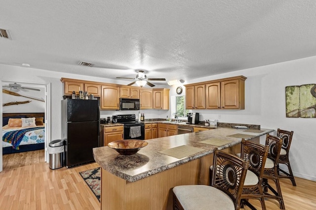 kitchen featuring ceiling fan, kitchen peninsula, light wood-type flooring, black appliances, and a breakfast bar area