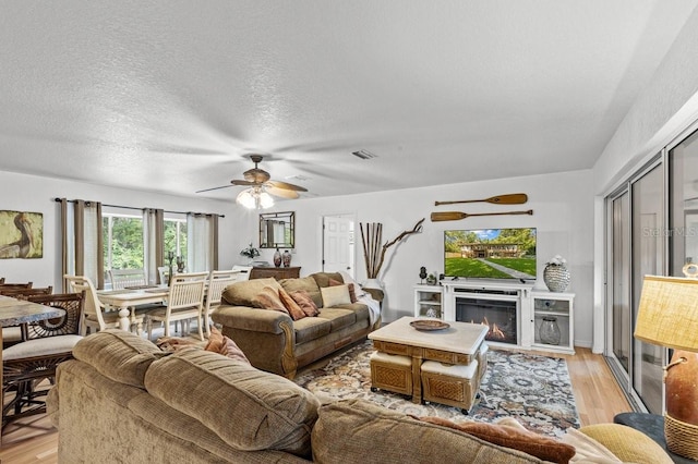 living room with plenty of natural light, ceiling fan, a textured ceiling, and light wood-type flooring