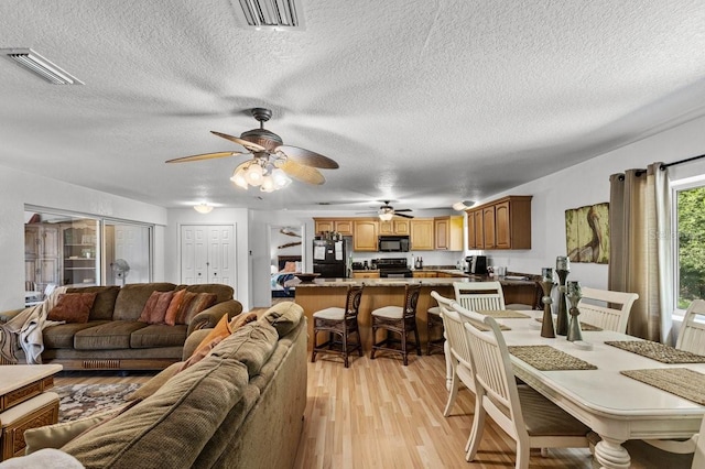 living room featuring ceiling fan, a textured ceiling, and light wood-type flooring