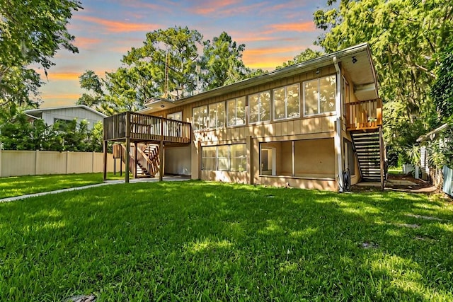 back house at dusk featuring a wooden deck and a yard