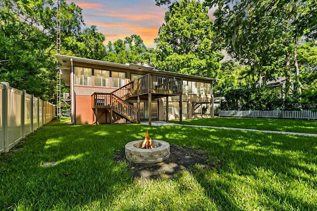 back house at dusk with an outdoor fire pit, a lawn, and a wooden deck