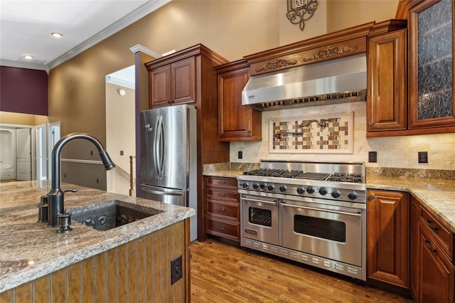 kitchen featuring sink, backsplash, stainless steel appliances, light stone countertops, and wall chimney range hood