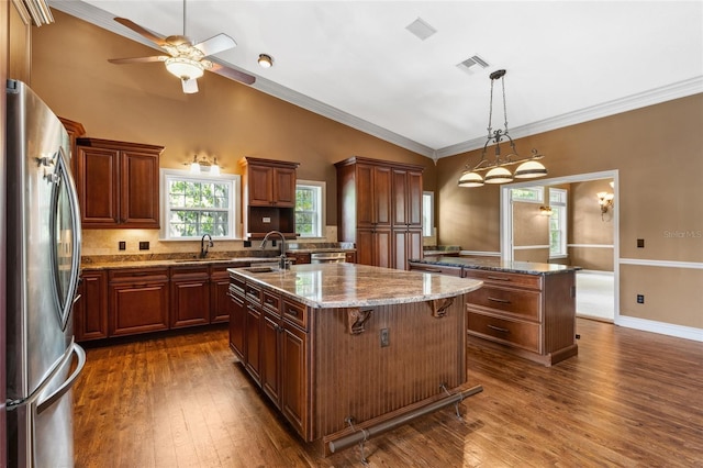 kitchen with sink, hanging light fixtures, stainless steel refrigerator, dark hardwood / wood-style floors, and an island with sink