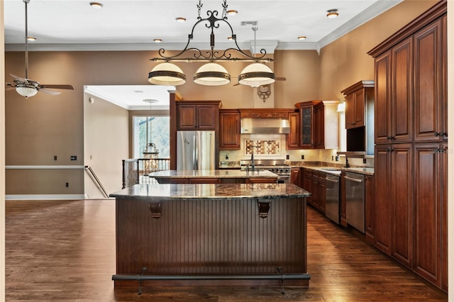 kitchen featuring wall chimney range hood, decorative light fixtures, a spacious island, and appliances with stainless steel finishes