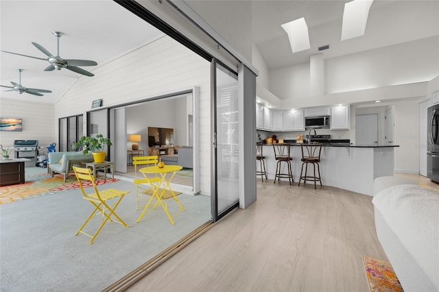 living room featuring a skylight, ceiling fan, high vaulted ceiling, and light hardwood / wood-style floors