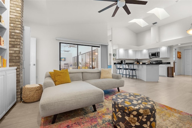 living room featuring light wood-type flooring, a skylight, high vaulted ceiling, and ceiling fan