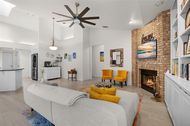 living room featuring ceiling fan, light wood-type flooring, high vaulted ceiling, and a brick fireplace