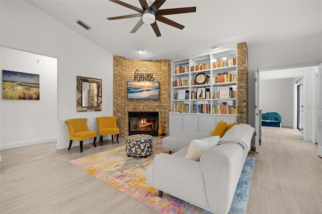 living room featuring light hardwood / wood-style flooring, vaulted ceiling, ceiling fan, built in shelves, and a fireplace