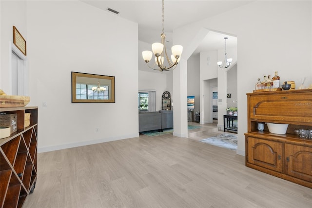 dining room with a towering ceiling, a notable chandelier, and light wood-type flooring