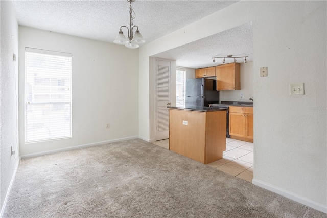 kitchen with hanging light fixtures, black fridge, light carpet, and a healthy amount of sunlight