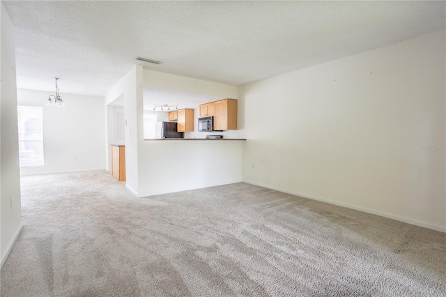 unfurnished living room featuring a textured ceiling, light carpet, and an inviting chandelier