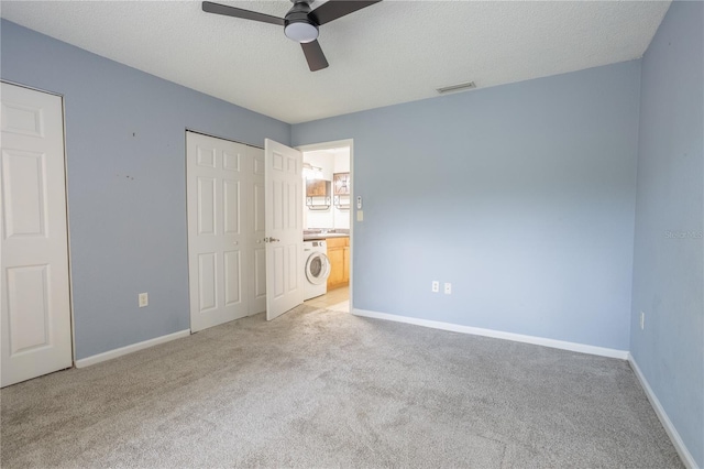 unfurnished bedroom featuring ceiling fan, a textured ceiling, washer / dryer, and light carpet