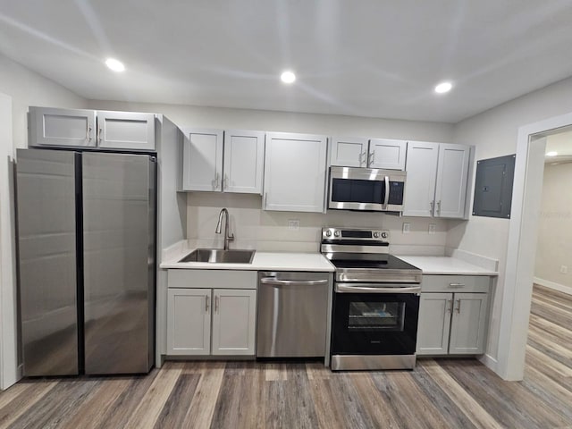 kitchen with wood finished floors, electric panel, a sink, stainless steel appliances, and light countertops